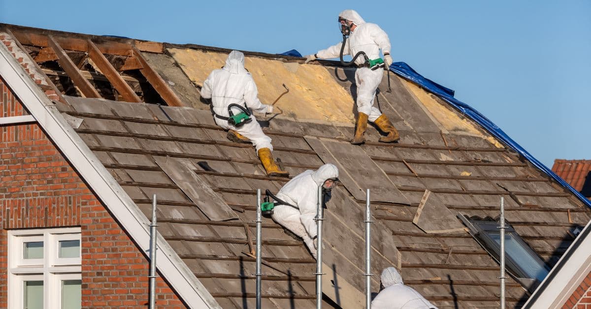 Licensed removalists in protective suits and respirators stripping an asbestos roof