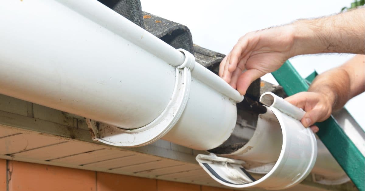 Roof plumber replacing a section of dirty, damaged guttering at the roof edge