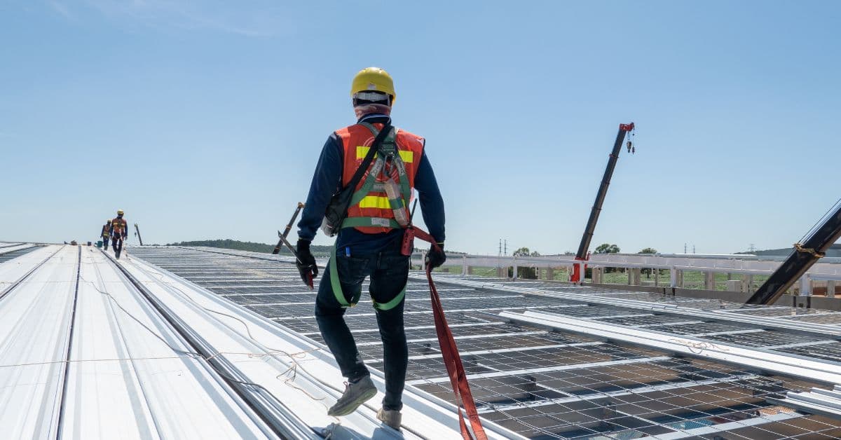 Harnessed roofer inspecting the surface of a large commercial metal roof