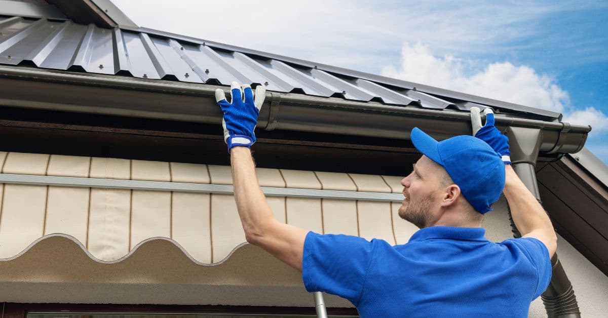 Roof plumber fitting new guttering along the edge of a dark metal roof