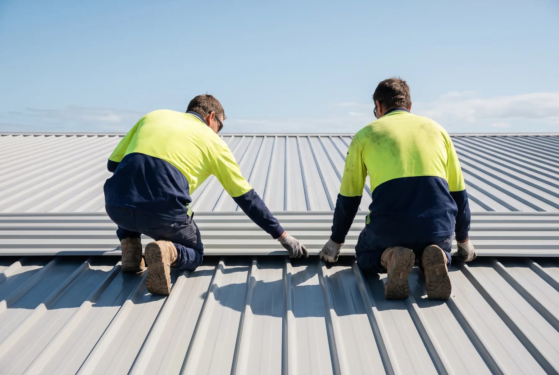 Two roofers working together to set a steel roof sheet